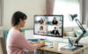 A woman sits at a desk in her living room taking notes while on a video conference call