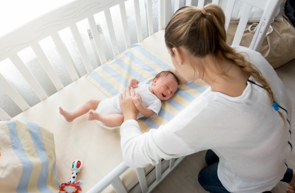 A mother lays her newborn in a crib.