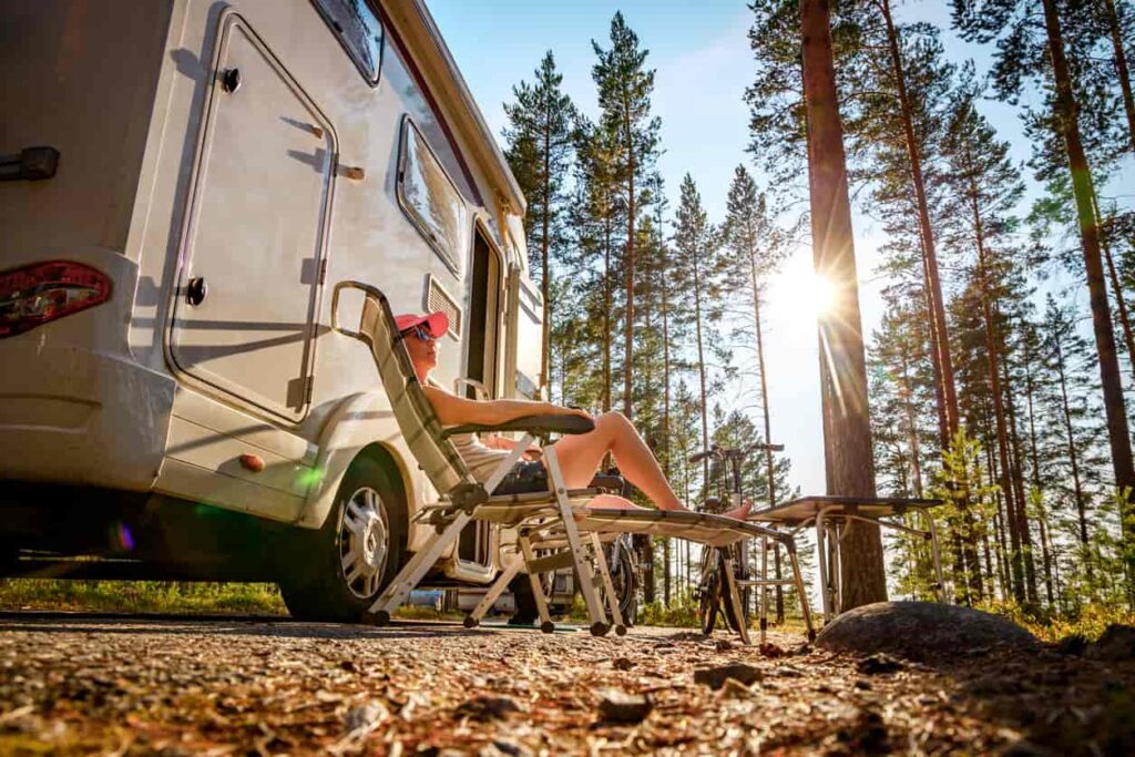A woman sits under the sun by her RV while camping.