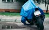 A motorbike covered with a tarp parked on wet grass in a rainstorm.