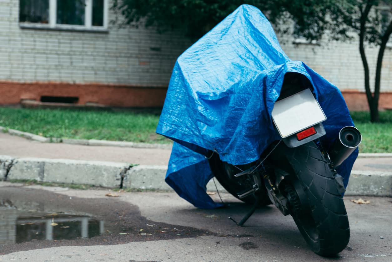 A motorbike covered with a tarp parked on wet grass in a rainstorm.