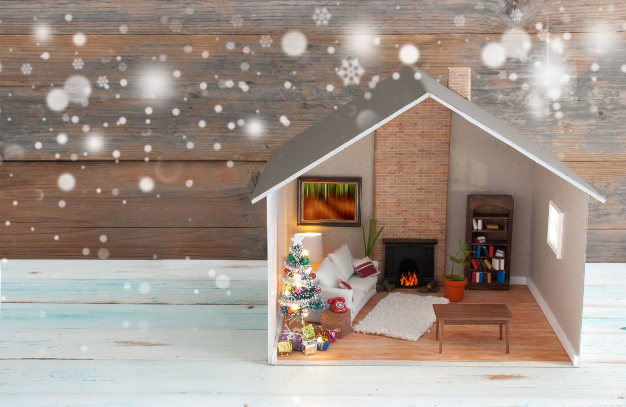 A miniature house is surrounded with snow and decorated for the holidays