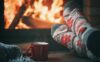 Someone crosses their feet in cozy socks in front of a warm fireplace in the winter.