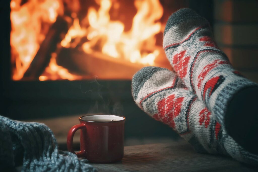 Someone crosses their feet in cozy socks in front of a warm fireplace in the winter.