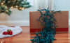 Green holiday lights hanging over the side of a box next to a Christmas tree.