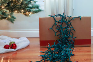 Green holiday lights hanging over the side of a box next to a Christmas tree.