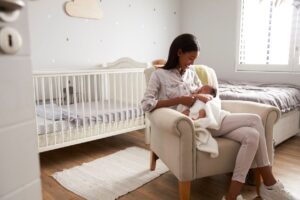 A woman and her newborn baby sit in their sunny home nursery.