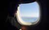 A man looks out the window of an airplane while traveling for work.