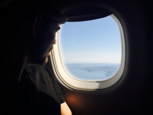 A man looks out the window of an airplane while traveling for work.