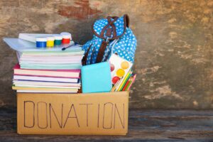 A box of school supplies labeled “donation” sits on a bench.