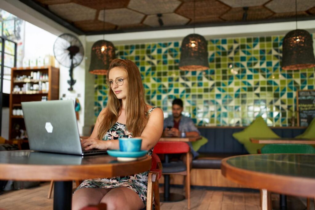 A woman smiles as she works remotely ain a coffee shop.