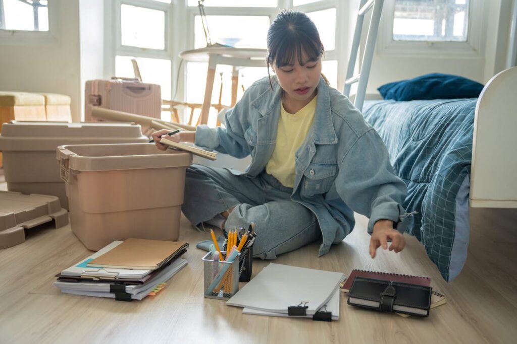 A woman organizing her room by sorting belongings and placing items into storage bins.