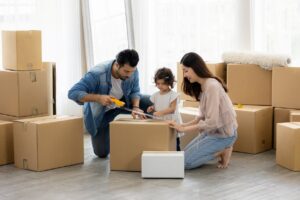 A family packing moving boxes together at home, taping boxes, and getting ready for a move with packing supplies.