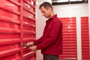 A person secures a padlock onto the latch of a closed corrugated metal storage unit door.